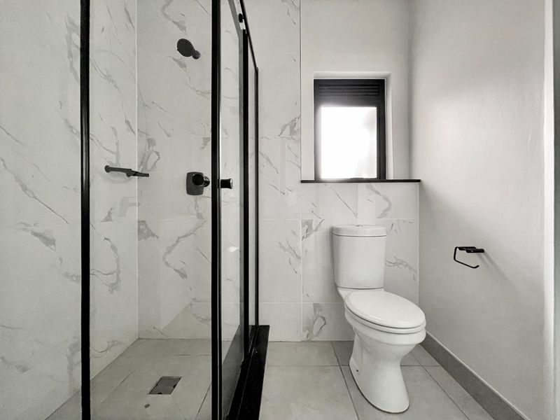 A modern, renovated bathroom featuring a walk-in shower with black-framed glass, marble-look wall tiles, and contemporary black hardware.