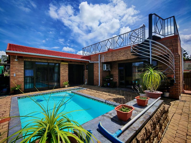 Outdoor pool area featuring a paved patio, brick exterior, and a spiral staircase leading to an upper-level roof terrace.