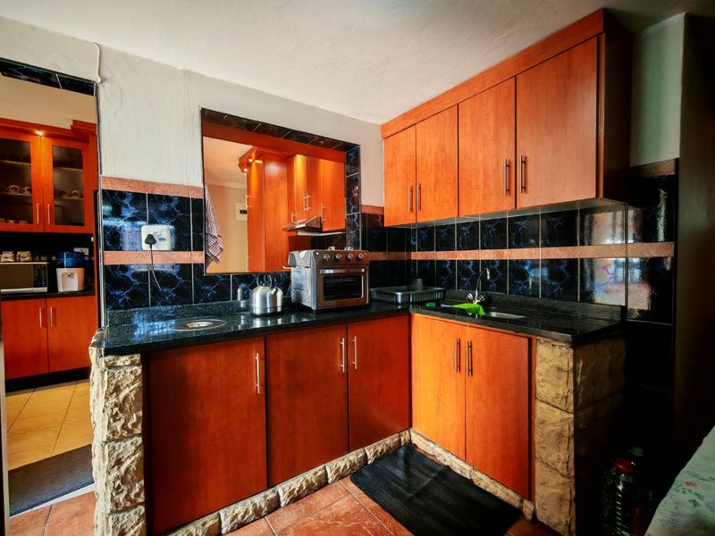 A functional kitchen featuring wooden cabinetry, granite countertops, and a decorative stone-clad base with a dark tiled backsplash.