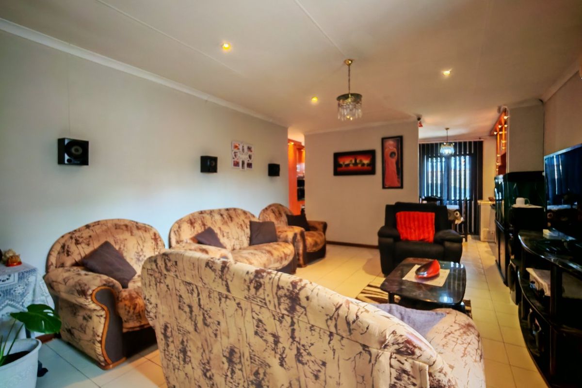A spacious living room featuring neutral tiled flooring, coved ceilings with recessed lighting, and a functional layout suitable for comfortable family living.