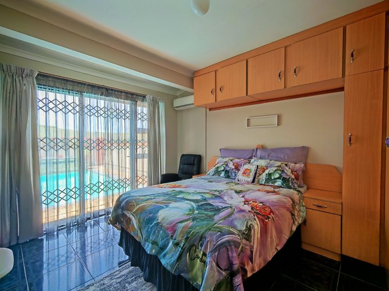 A bedroom featuring built-in wooden cupboards, tiled flooring, and a sliding glass door with a security gate providing direct access to the pool area.