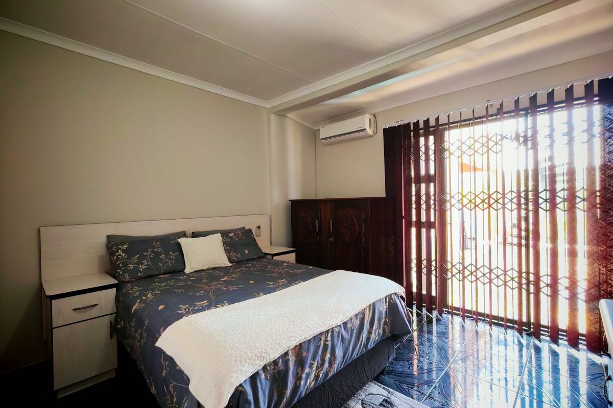 A bedroom featuring tiled flooring, a built-in headboard with integrated bedside tables, a split-system air conditioner, and a security gate leading to the exterior.