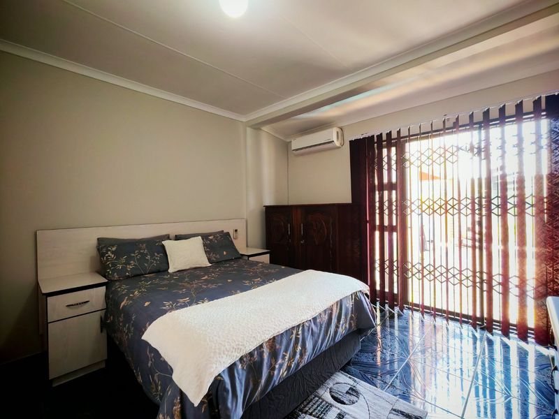 A bedroom featuring tiled flooring, a built-in headboard with integrated bedside tables, a split-system air conditioner, and a security gate leading to the exterior.