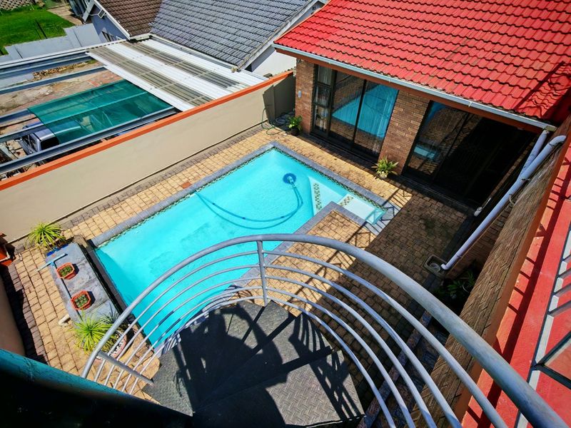 An elevated view of a private swimming pool area featuring a paved patio, brick exterior walls, and a metal spiral staircase.