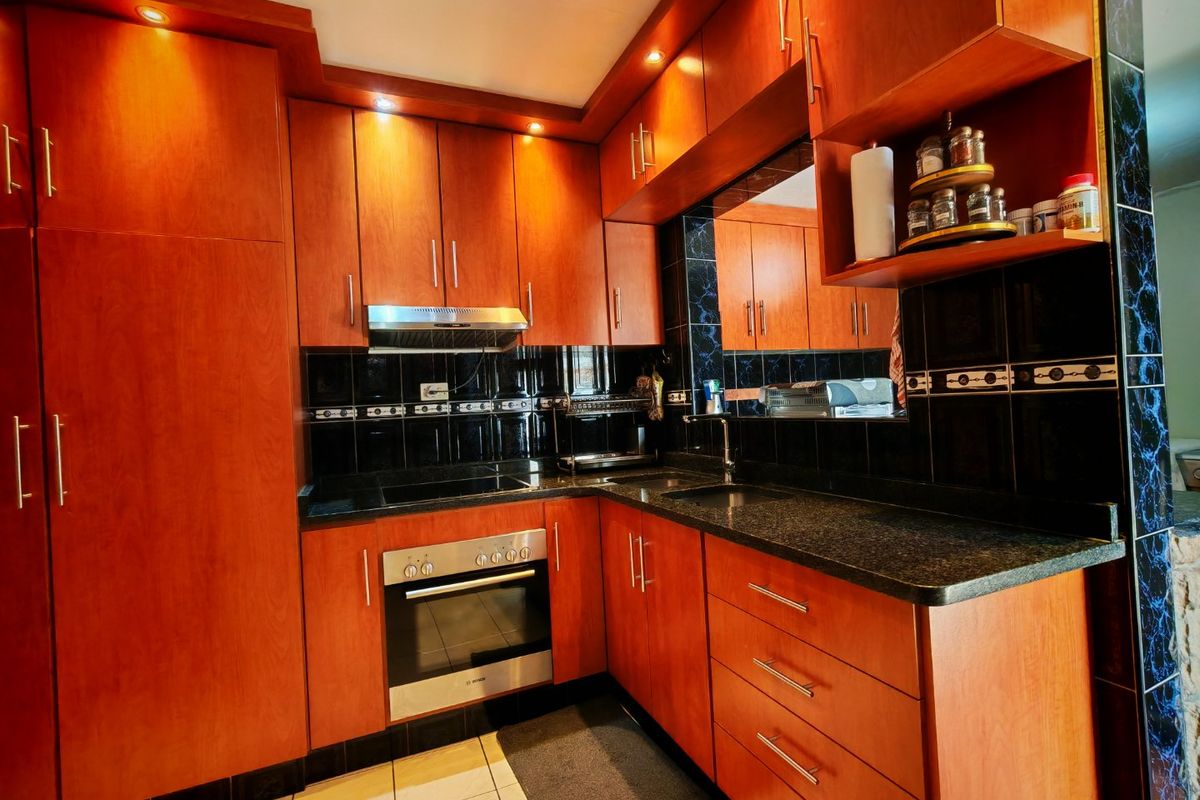 A well-maintained kitchen featuring warm-toned wooden cabinetry, granite countertops, a built-in oven, electric hob, and a stylish black tiled backsplash.
