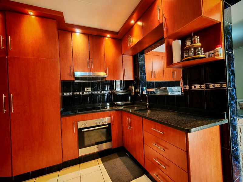 A well-maintained kitchen featuring warm-toned wooden cabinetry, granite countertops, a built-in oven, electric hob, and a stylish black tiled backsplash.