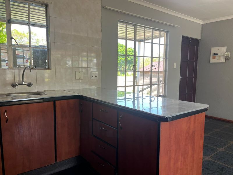 A functional kitchen featuring wooden cabinetry, laminate countertops, a stainless steel sink, and tiled backsplash, with natural light from multiple windows.