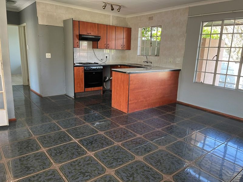 An empty kitchen featuring wooden cabinetry, built-in oven and hob, tiled flooring, and a breakfast counter, offering a functional layout ready for updates.