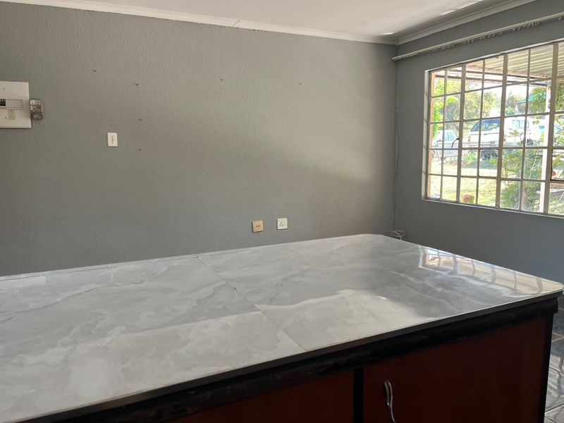 A functional kitchen space featuring a central island with a marble-effect countertop and security-barred windows, offering a blank canvas for updates.