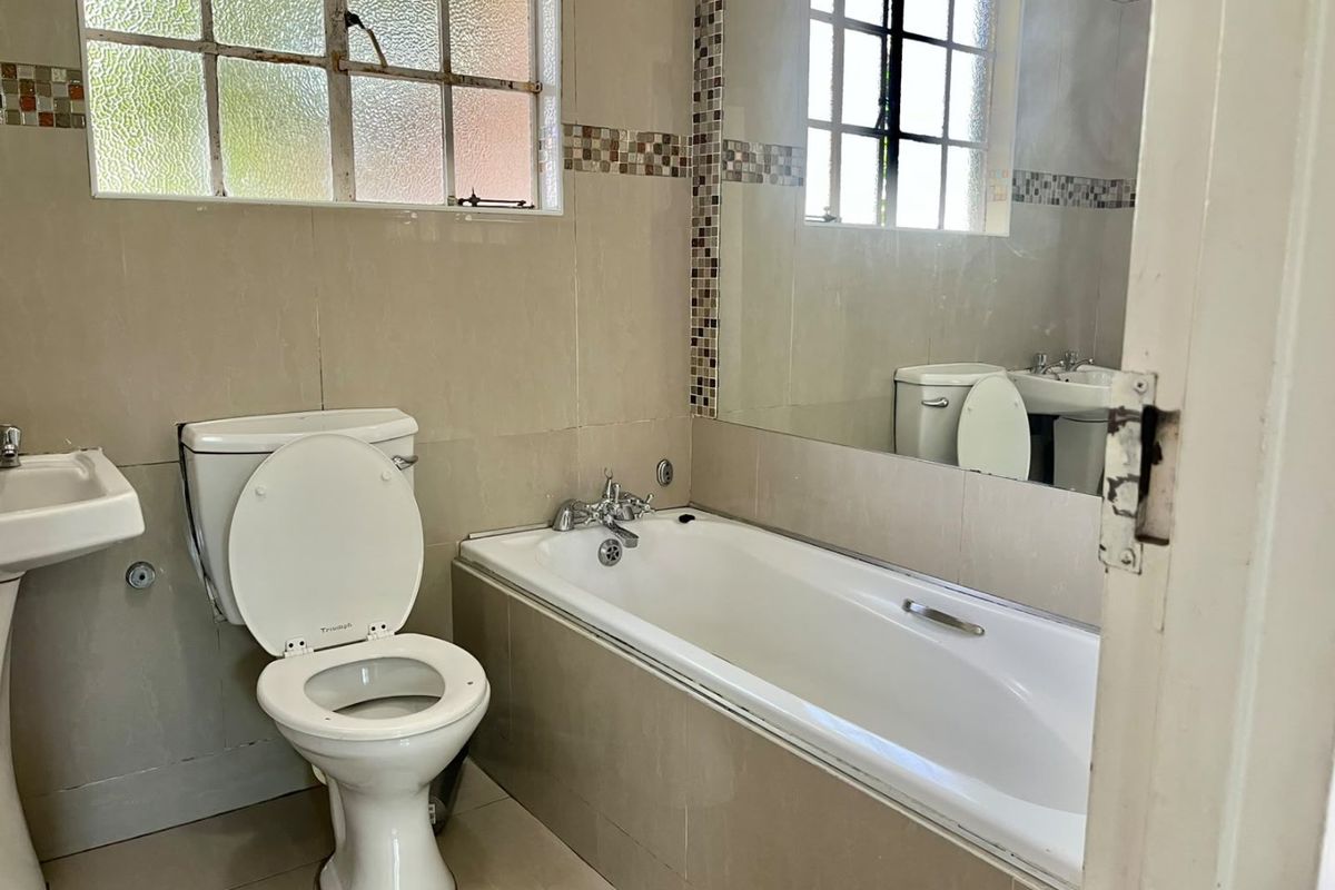 A functional bathroom featuring a pedestal basin, built-in bathtub, and tiled finishes, offering a clean space ready for modern updates.