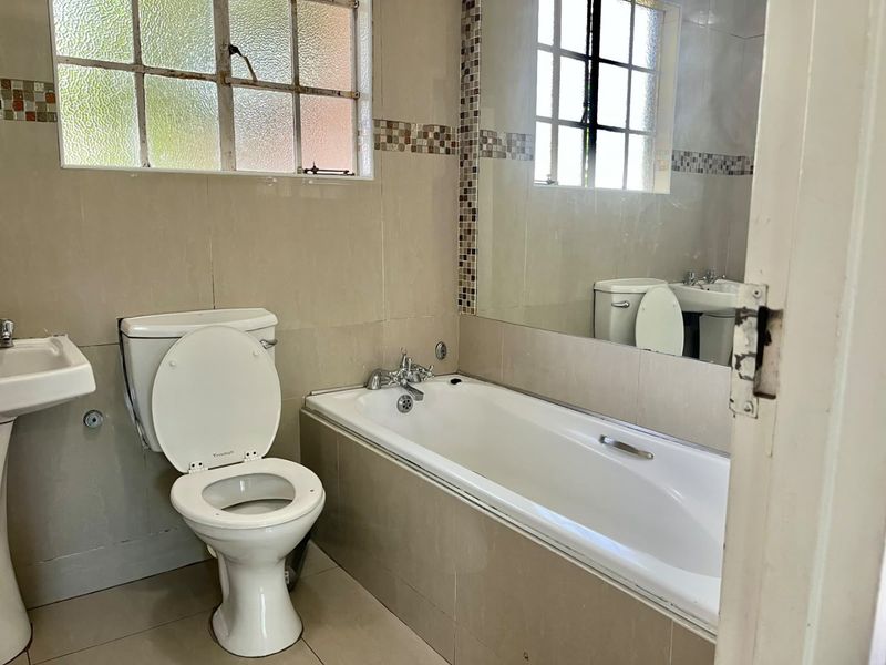 A functional bathroom featuring a pedestal basin, built-in bathtub, and tiled finishes, offering a clean space ready for modern updates.