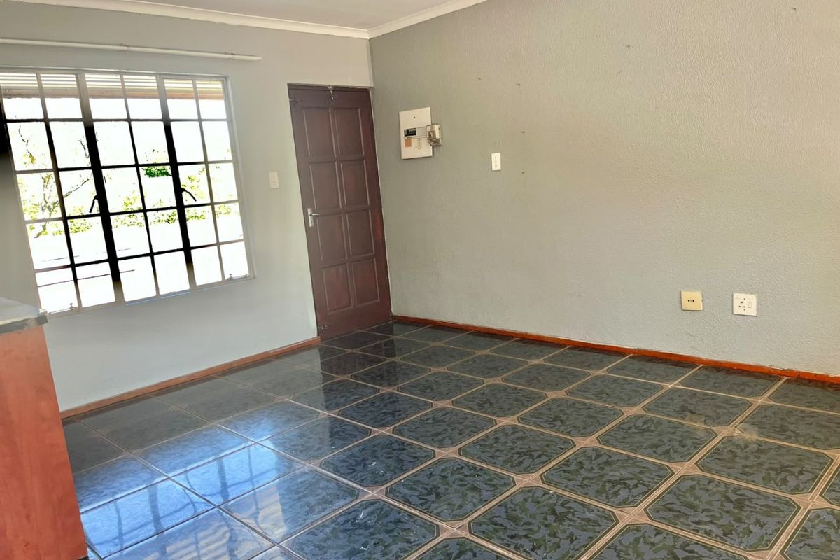 An empty living area featuring dark patterned floor tiles, a grid-style window, and a timber door, providing a blank canvas for renovation.
