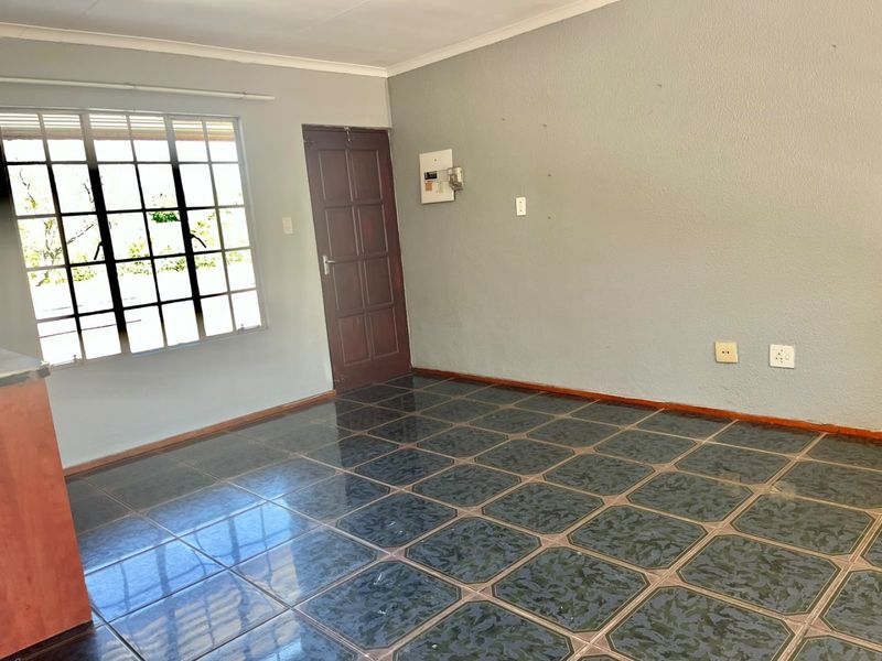 An empty living area featuring dark patterned floor tiles, a grid-style window, and a timber door, providing a blank canvas for renovation.
