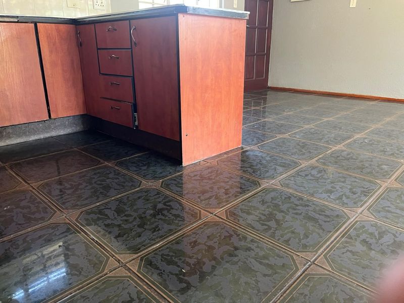 A kitchen area featuring dark patterned floor tiles and wooden cabinetry, currently vacant and in need of minor repairs and cosmetic updates.