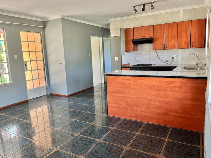 Open plan kitchen and living area featuring wooden cabinetry, built-in hob, extractor fan, and tiled flooring with direct access to the exterior.