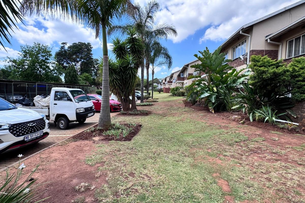 Exterior view of the apartment complex rear facade featuring brick detailing, security-fitted windows, and a shared garden area with paved parking.