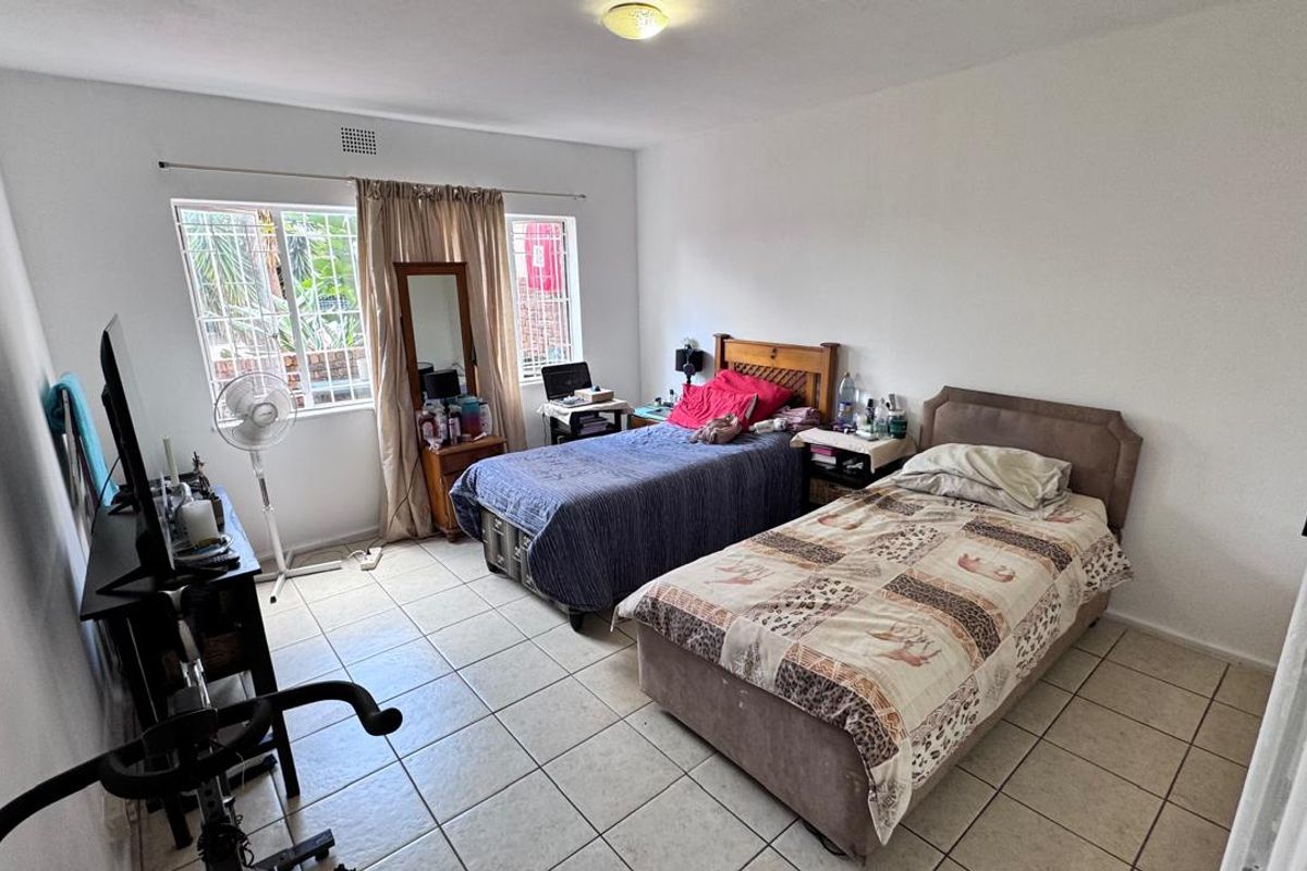 A functional bedroom featuring tiled flooring and windows fitted with security bars, providing a practical space for rest.