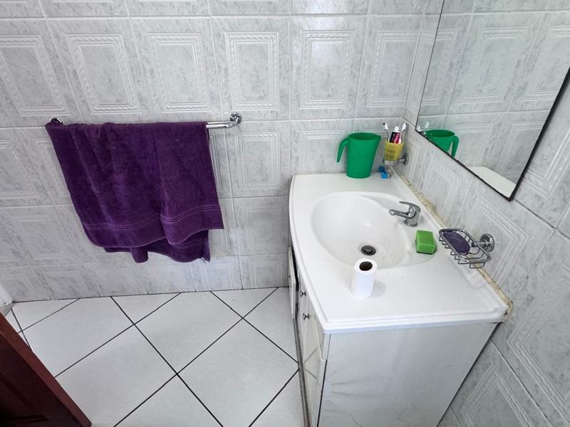 A functional bathroom featuring a vanity cabinet with a ceramic basin, chrome faucet, wall mirror, and tiled surfaces throughout.