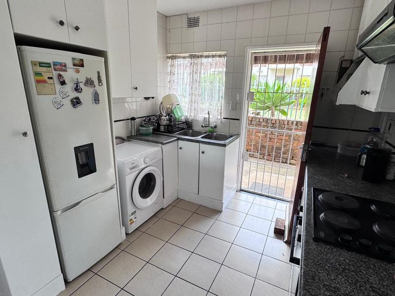 Functional kitchen featuring built-in cabinetry, electric hob, extractor fan, and tiled finishes with direct access to an exterior area.
