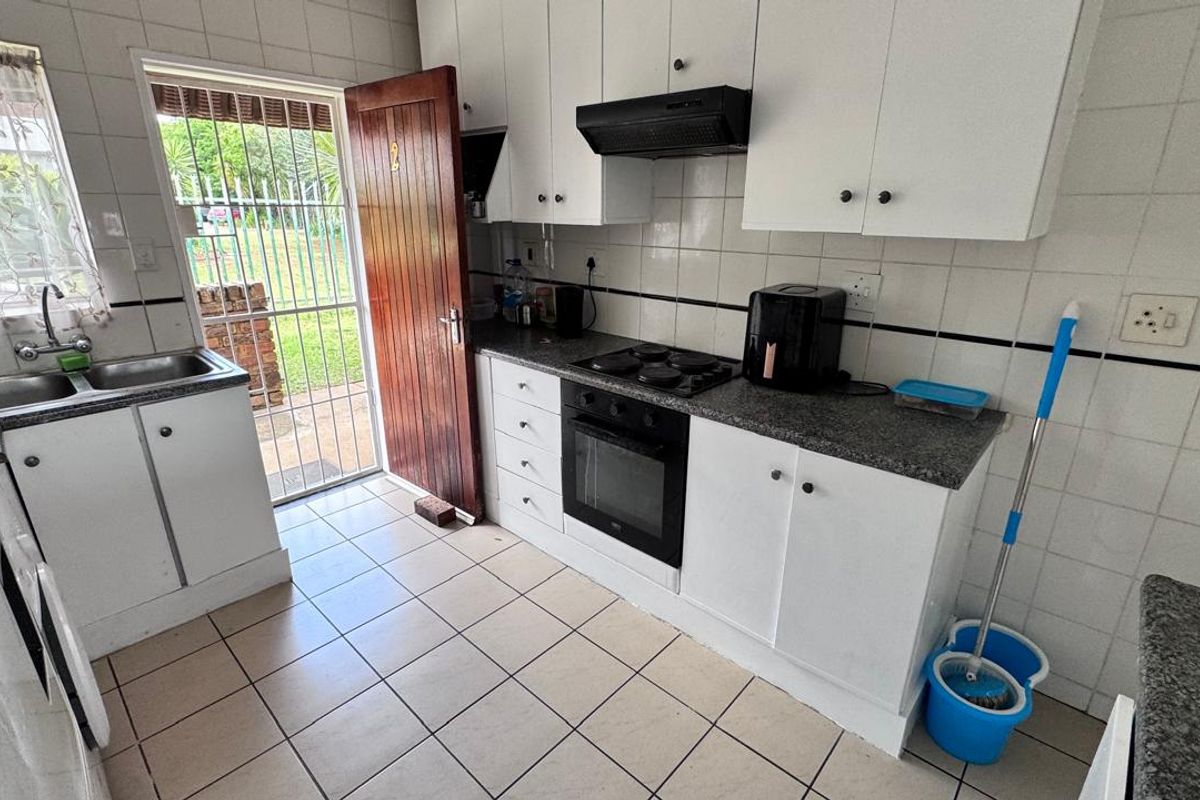 Functional kitchen featuring white cabinetry, granite countertops, built-in oven, hob, extractor fan, and direct access to the exterior via a security gate.