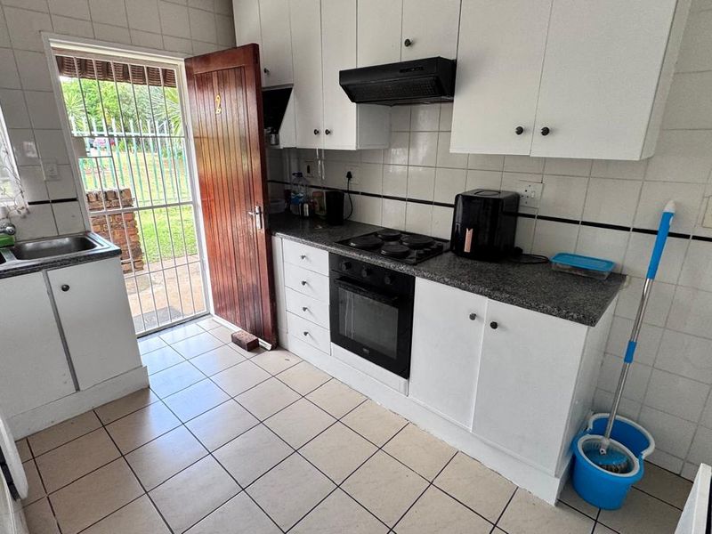 Functional kitchen featuring white cabinetry, granite countertops, built-in oven, hob, extractor fan, and direct access to the exterior via a security gate.