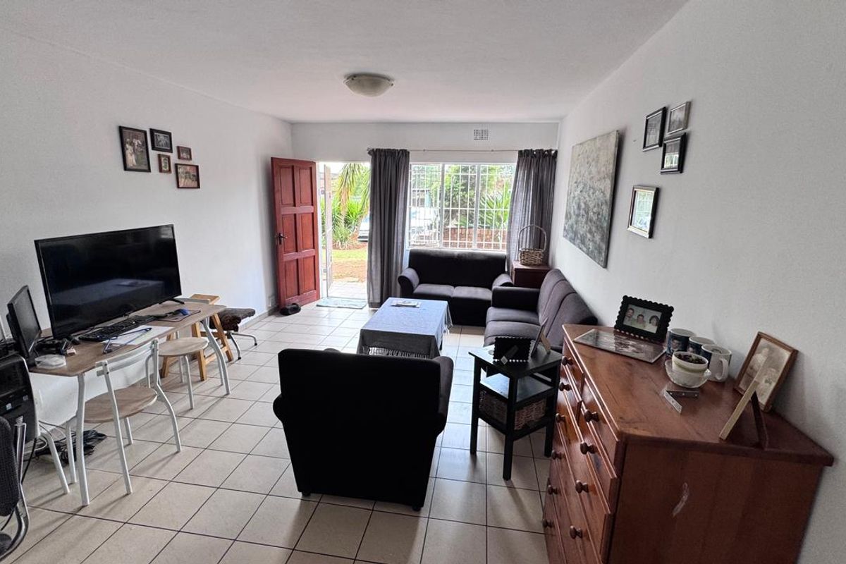 A functional living room featuring tiled flooring, a security gate leading to the exterior, and a window fitted with security bars.