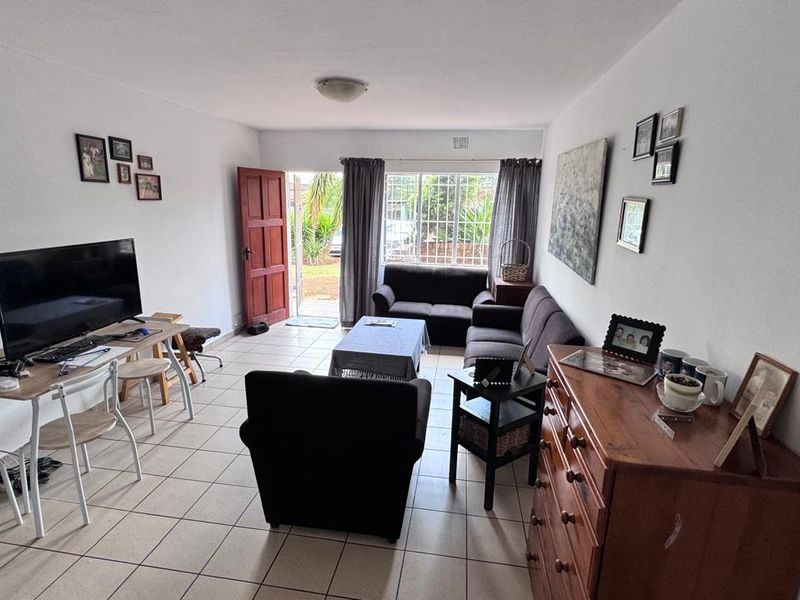 A functional living room featuring tiled flooring, a security gate leading to the exterior, and a window fitted with security bars.