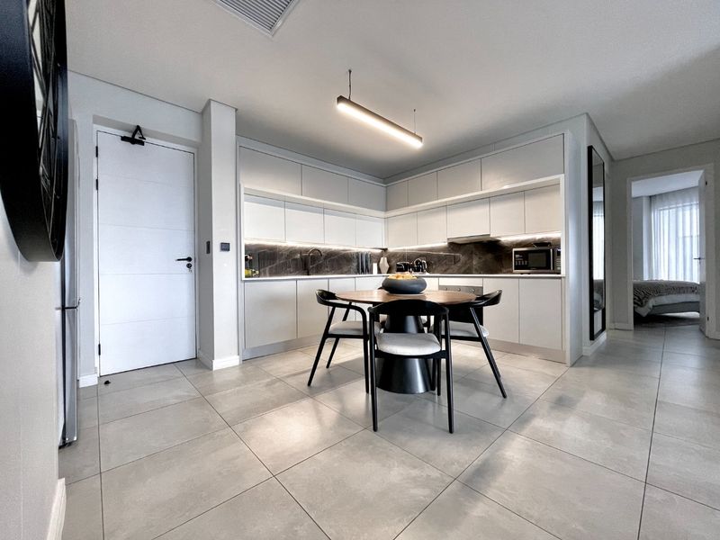 Modern open-plan kitchen featuring sleek handleless cabinetry, stone backsplash, integrated appliances, and large format floor tiles, seamlessly flowing into the dining area.