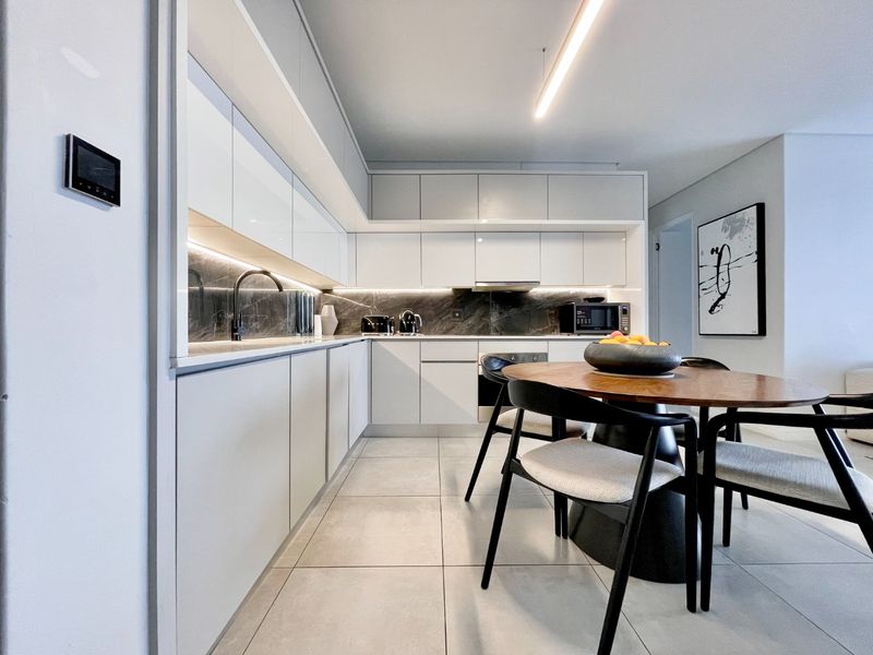 Modern open-plan kitchen featuring sleek white cabinetry, stone backsplash, integrated appliances, and high-quality tiled flooring with contemporary lighting.