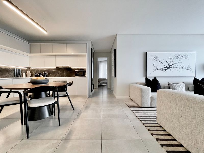 Modern open-plan living area featuring a sleek kitchen with stone backsplash, integrated appliances, and neutral tiled flooring throughout the connected dining and lounge space.