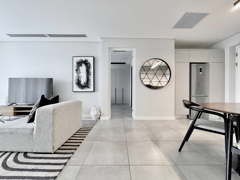 Modern open-plan living and dining area featuring sleek tiled flooring, integrated kitchen cabinetry, and recessed ceiling climate control systems.