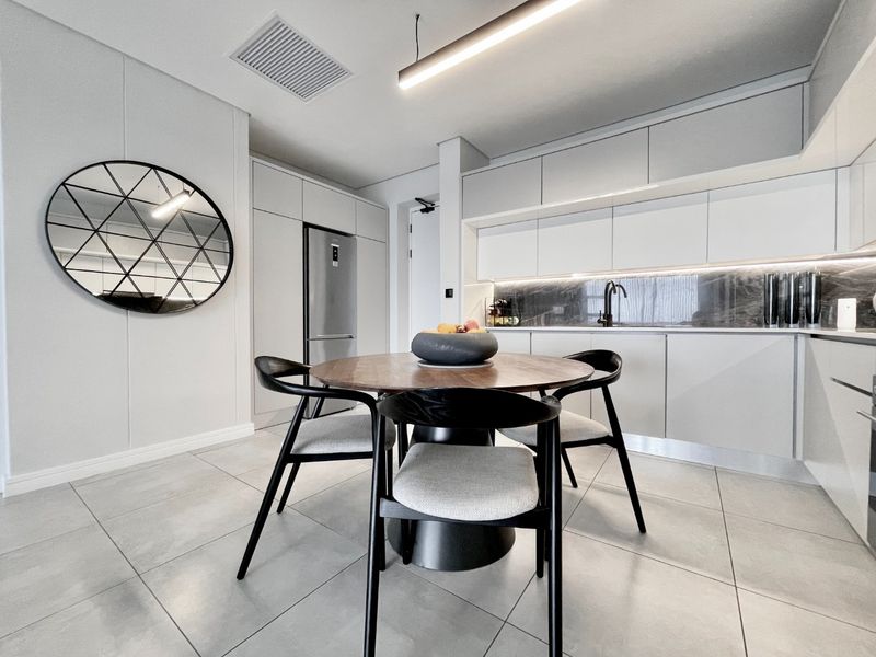 Modern open-plan kitchen featuring sleek handleless cabinetry, stone splashback, integrated appliances, and large format floor tiles in a contemporary apartment setting.