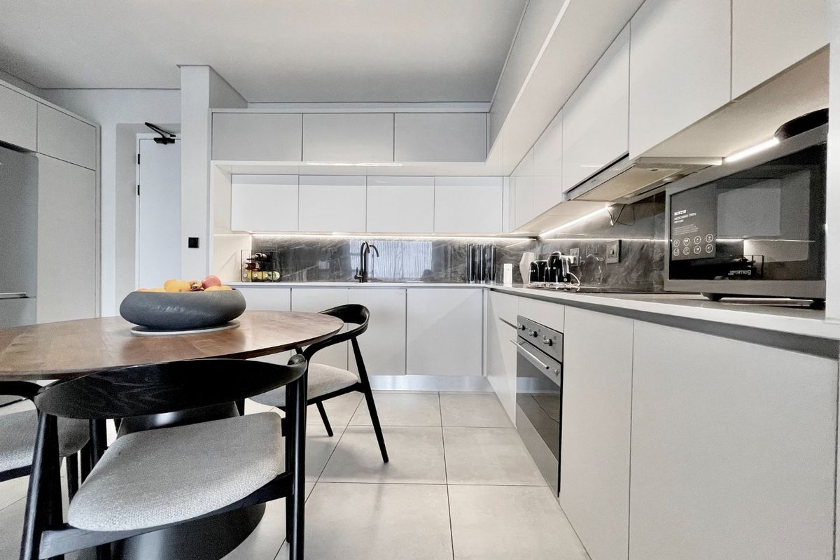 Modern kitchen featuring sleek white cabinetry, stone splashback, integrated appliances, and high-quality tiled flooring in a contemporary open-plan layout.
