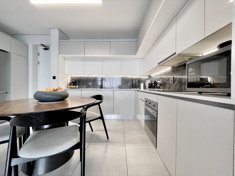 Modern kitchen featuring sleek white cabinetry, stone splashback, integrated appliances, and high-quality tiled flooring in a contemporary open-plan layout.