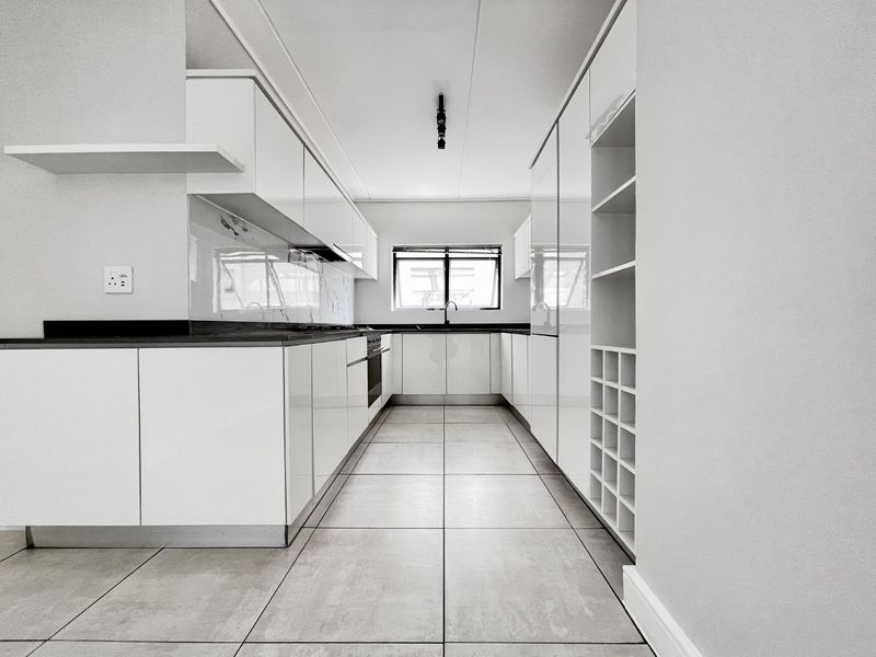 Modern galley-style kitchen featuring high-gloss white cabinetry, dark stone countertops, integrated oven, hob, and sleek tiled flooring.