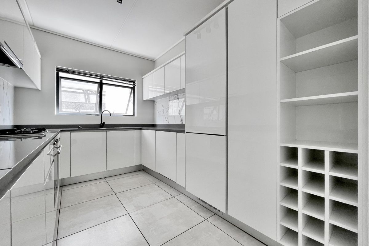 Modern, minimalist kitchen featuring sleek white cabinetry, integrated appliances, stone countertops, and a dedicated wine rack, finished with contemporary tiled flooring.