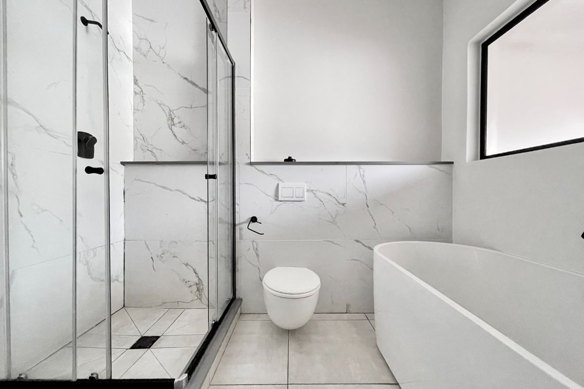 Modern bathroom featuring a walk-in shower with glass enclosure, a sleek freestanding bathtub, and a wall-hung toilet with marble-look tile finishes.