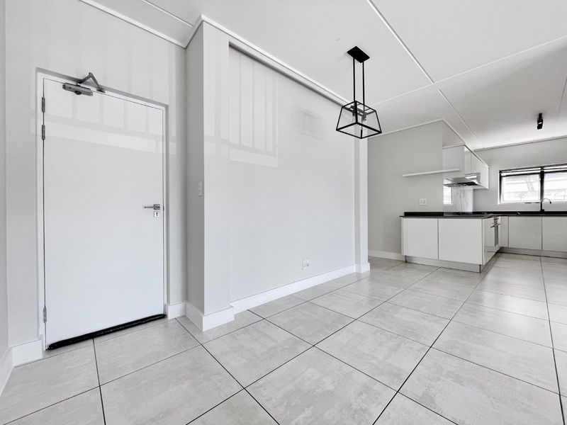 A bright, modern open-plan living and kitchen area featuring neutral tiled flooring, contemporary cabinetry, and clean finishes throughout.