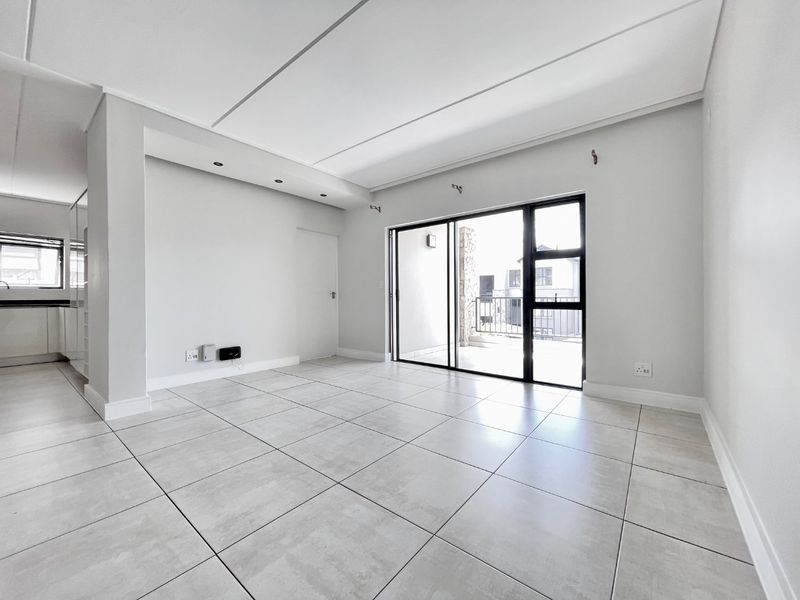 Bright and spacious open-plan living area featuring neutral tiled flooring, recessed lighting, and large sliding glass doors leading to an outdoor balcony.