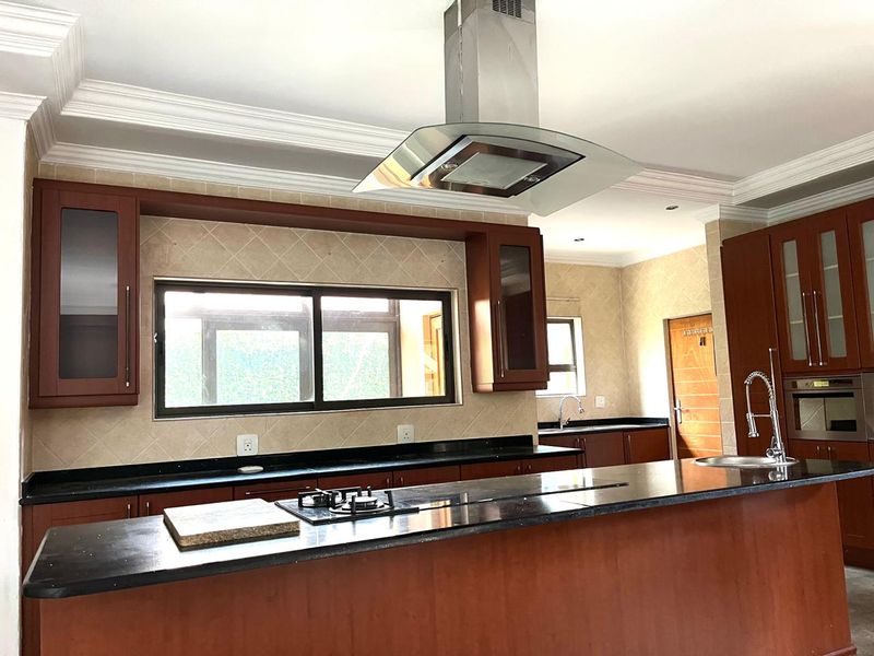 Spacious kitchen featuring dark wood cabinetry, granite countertops, a central island with a gas hob, and a stainless steel extractor fan.