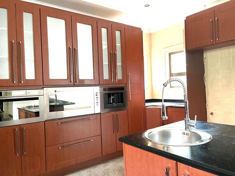 A functional kitchen featuring wood-finish cabinetry, granite countertops, a central island with a sink, and integrated built-in appliances.