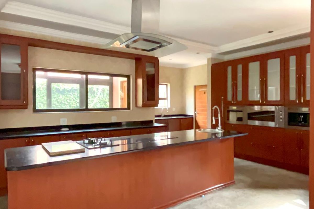 Spacious kitchen featuring dark wood cabinetry, granite countertops, a central island with a gas hob, and integrated stainless steel appliances.
