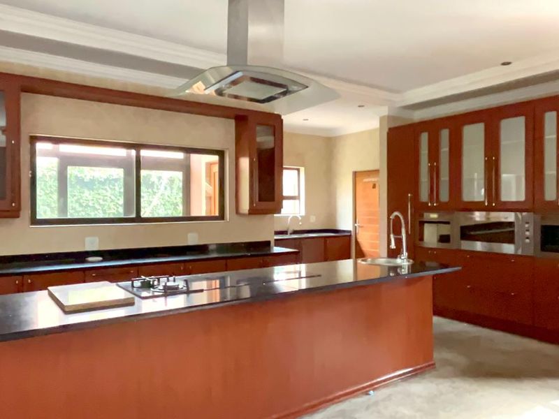 Spacious kitchen featuring dark wood cabinetry, granite countertops, a central island with a gas hob, and integrated stainless steel appliances.