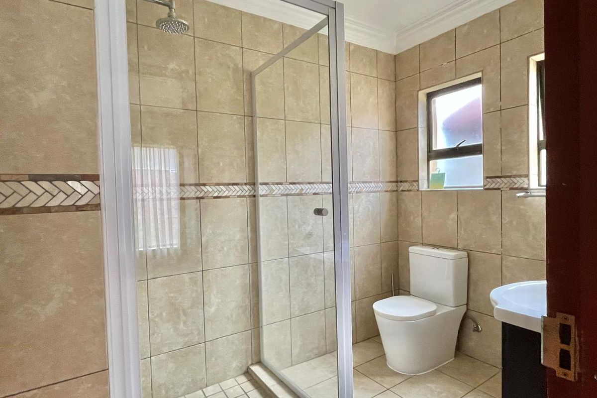 A clean, functional bathroom featuring a glass-enclosed shower, modern toilet, and vanity with neutral floor-to-ceiling tiling and a decorative accent border.