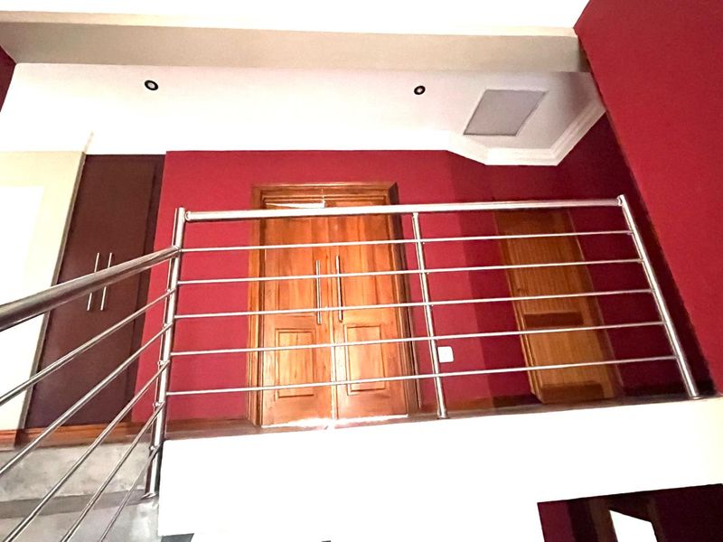 A landing area featuring a stainless steel balustrade, recessed lighting, and wooden doors, finished with bold red wall accents.