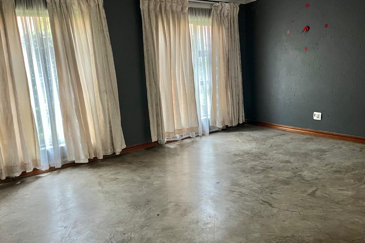 An empty living room featuring polished concrete floors, dark painted walls, and large windows with curtains.
