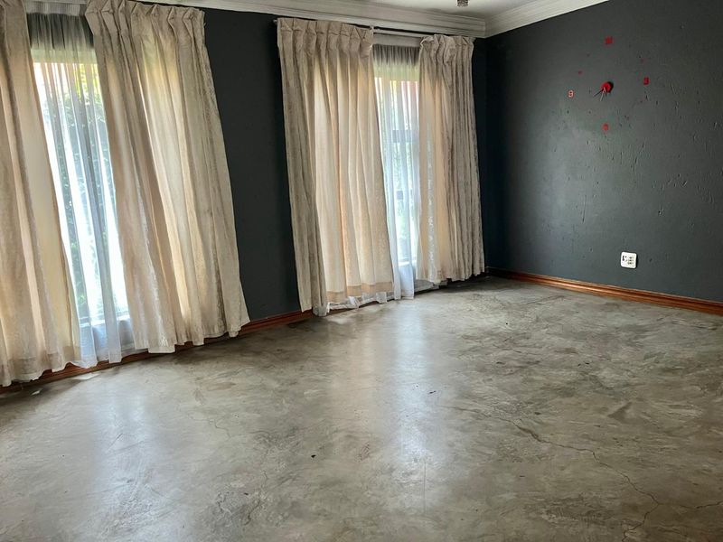 An empty living room featuring polished concrete floors, dark painted walls, and large windows with curtains.