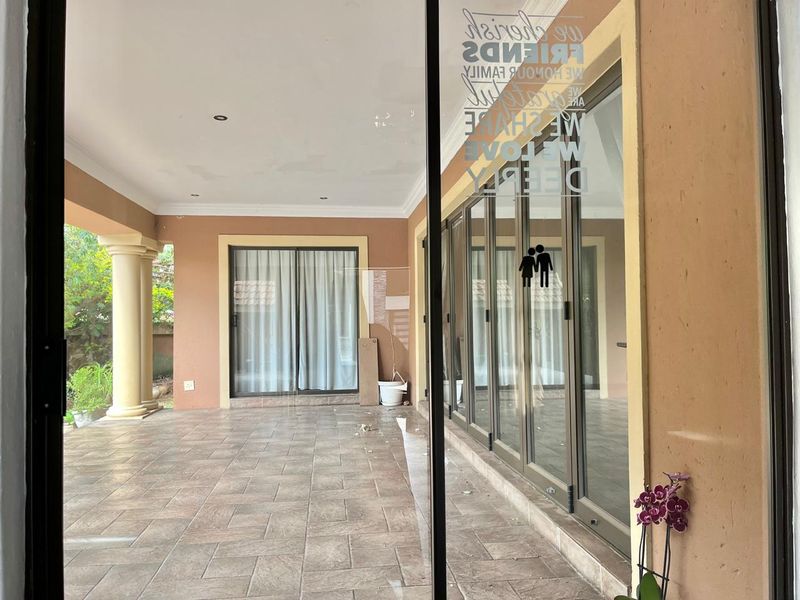 A spacious covered patio featuring tiled flooring, decorative columns, and large sliding glass doors, offering a versatile outdoor entertainment area.