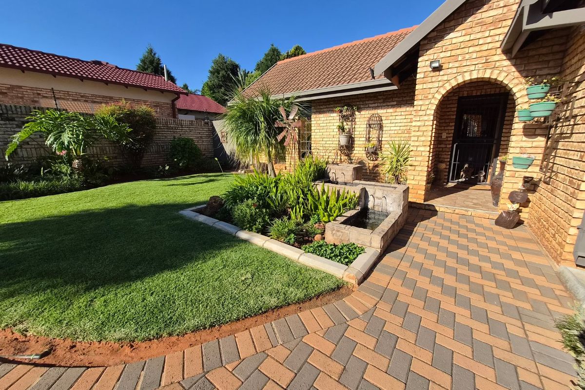 A well-maintained rear garden featuring a paved walkway, manicured lawn, and a built-in stone water feature adjacent to the brick house facade.