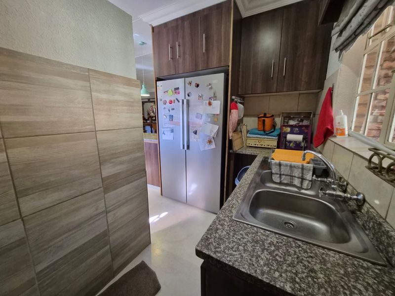 A functional scullery area featuring a double bowl stainless steel sink, granite countertops, and ample built-in cabinetry for storage.